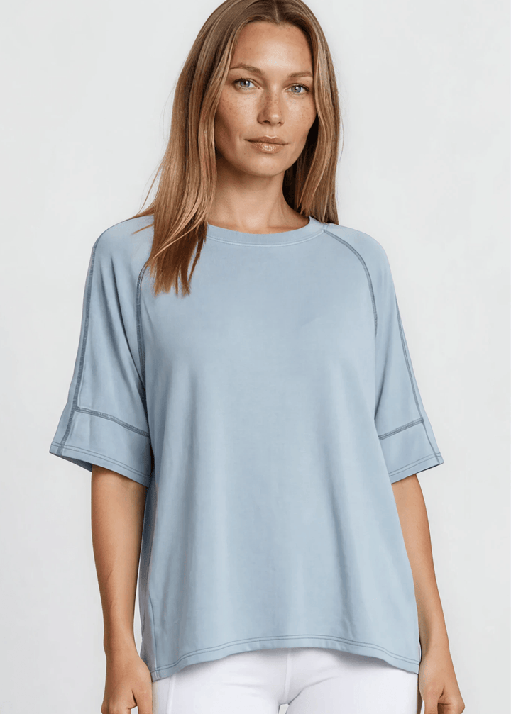  Evelyn Exposed Stitch Tee in Denim Blue. Oversized boxy fit, 3/4 raglan sleeves, contrast topstitching, super soft. Made in USA. Sizes S–XL.