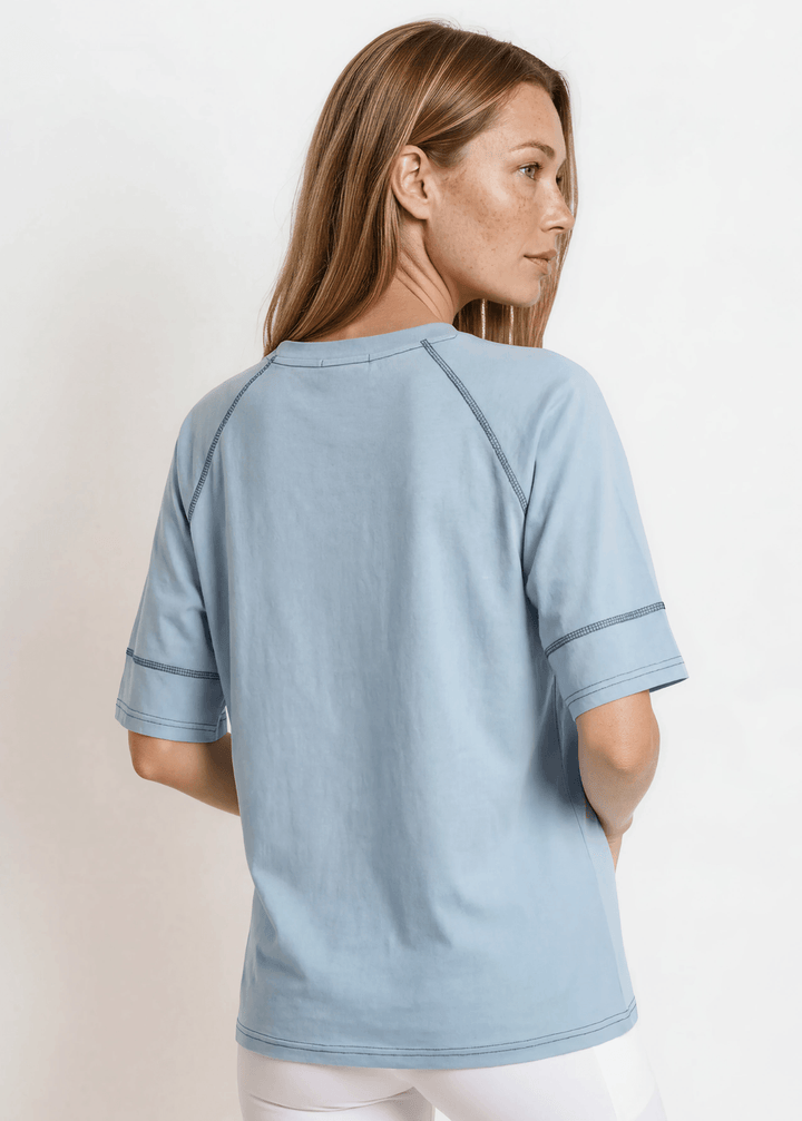  Evelyn Exposed Stitch Tee in Denim Blue. Oversized boxy fit, 3/4 raglan sleeves, contrast topstitching, super soft. Made in USA. Sizes S–XL.