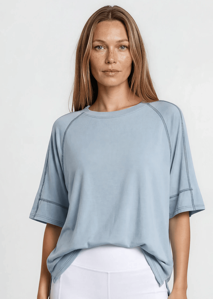  Evelyn Exposed Stitch Tee in Denim Blue. Oversized boxy fit, 3/4 raglan sleeves, contrast topstitching, super soft. Made in USA. Sizes S–XL.