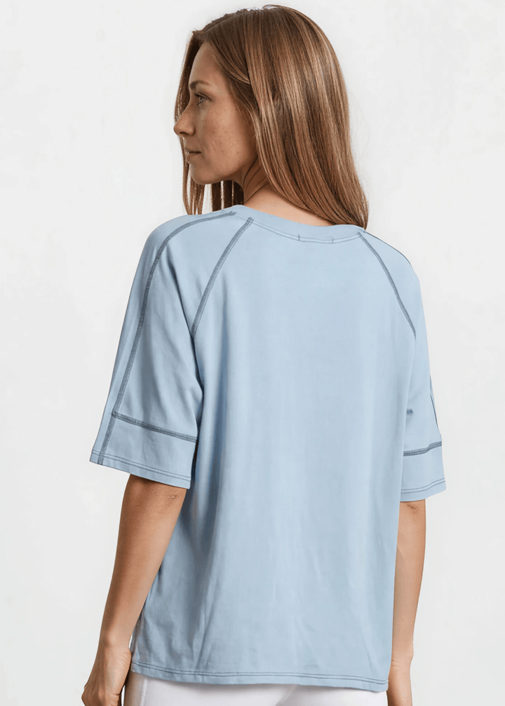  Evelyn Exposed Stitch Tee in Denim Blue. Oversized boxy fit, 3/4 raglan sleeves, contrast topstitching, super soft. Made in USA. Sizes S–XL.