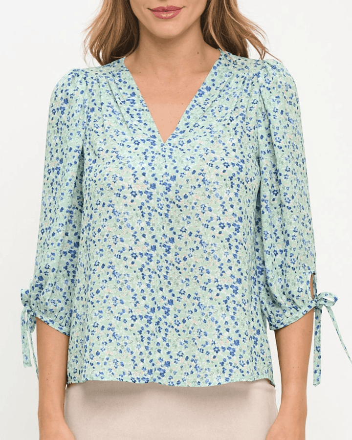 Delilah Ditsy Floral Top in Sage. V-neck, 3/4 tie sleeves, relaxed fit, 100% polyester. Feminine floral blouse made in the USA. Sizes S–L.
