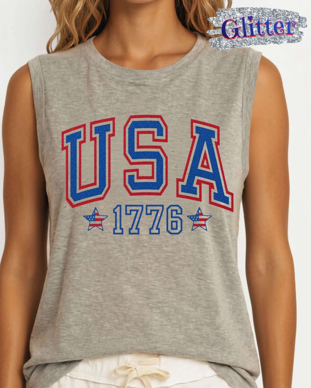 Glitter USA varsity graphic muscle tee with 1776 & flag star accents. Made in USA, relaxed fit, 75% cotton. Perfect for 4th of July. Sizes S-L.