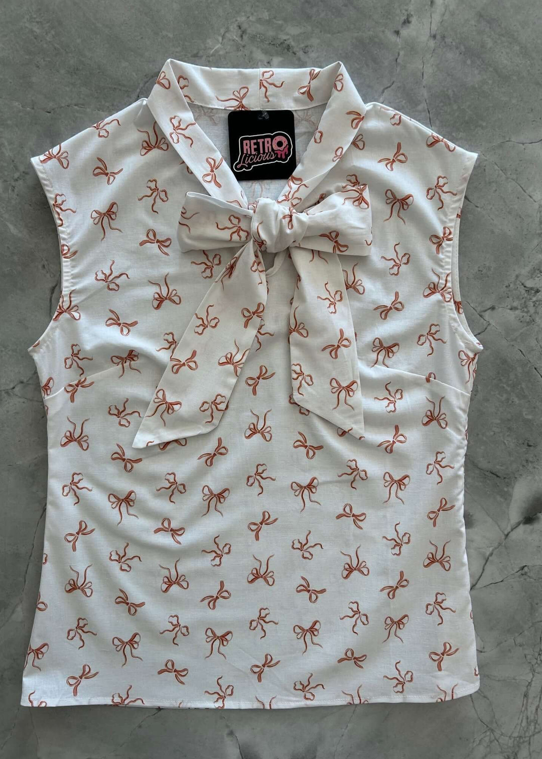 Vintage Style Tops This top is for the vintage lover at heart! Now available in our Pink Bows print. This 100% cotton top features bust darts for a flattering silhouette, a side zippered closure for ease of wear, and an oversized bow at the neckline for that perfect 1950&