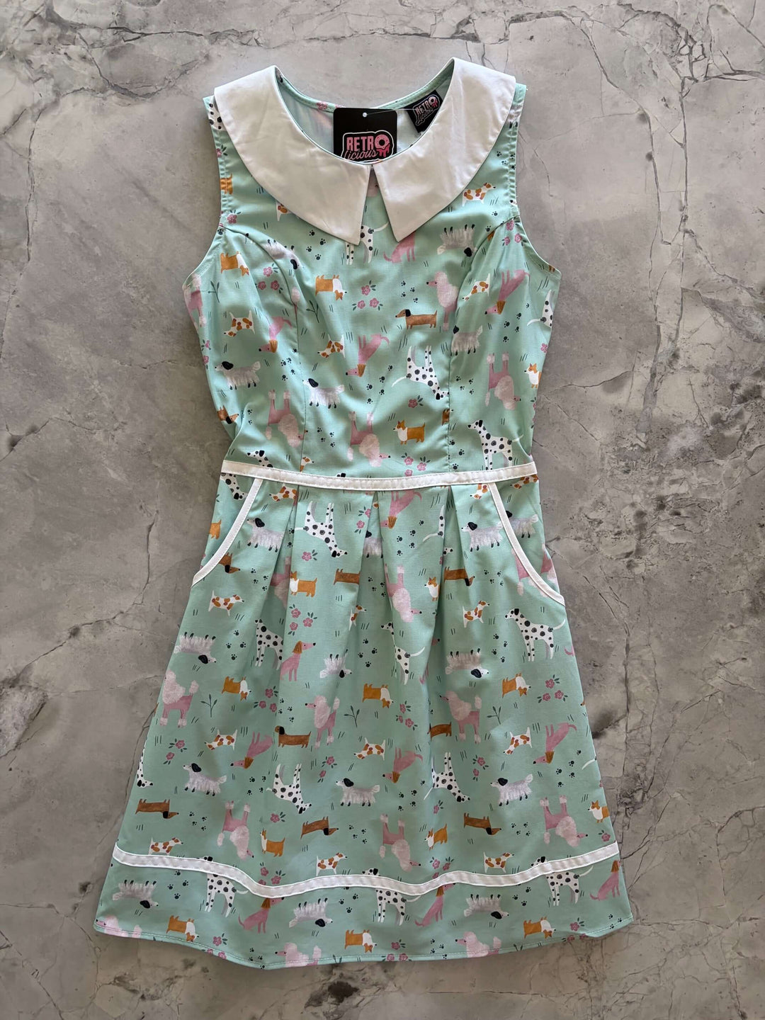 Shop the Dogs Collared Dress by Retrolicious — 60s-style A-line, dog print, Peter Pan collar, pockets, 100% cotton. Made in USA. Sizes XS–4X.