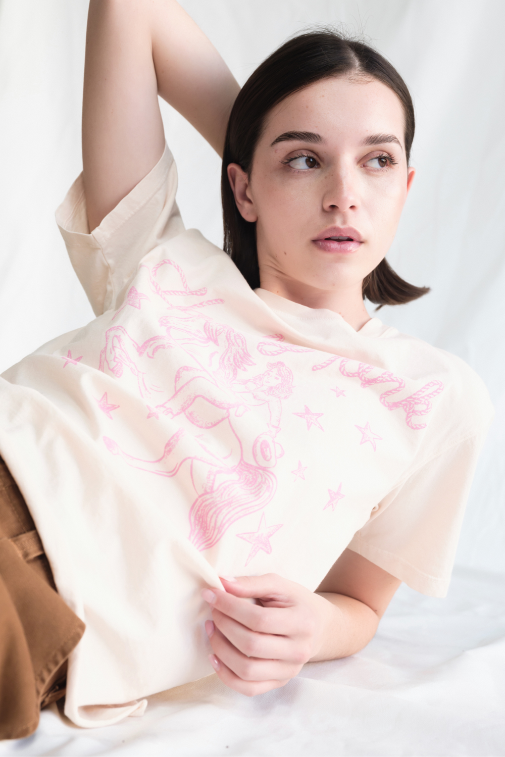 Shop the Honky Tonk Cowgirl Tee — a relaxed-fit crewneck in vanilla white with a pink cowgirl print. 100% cotton, sizes XS–XL.