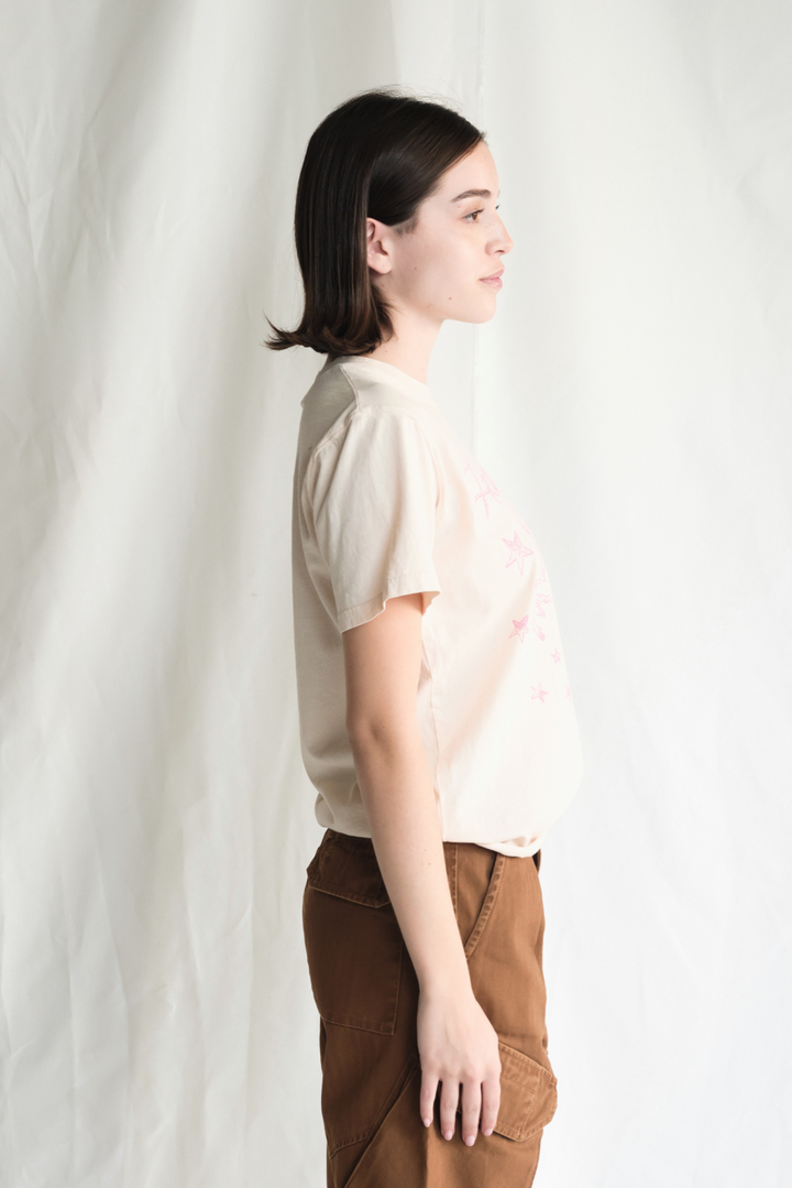 Shop the Honky Tonk Cowgirl Tee — a relaxed-fit crewneck in vanilla white with a pink cowgirl print. 100% cotton, sizes XS–XL.