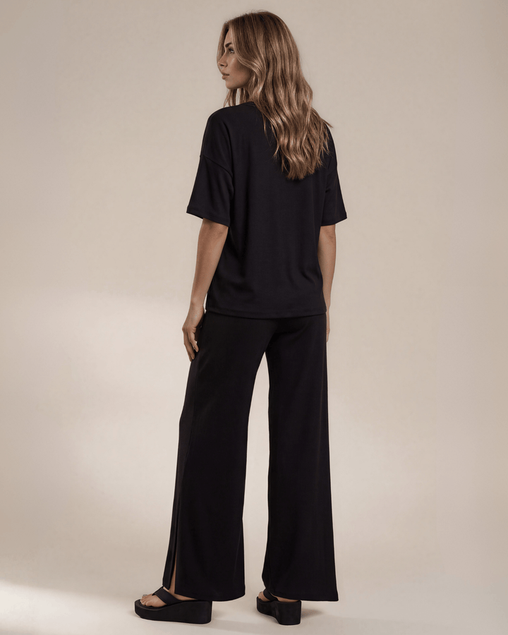 "Black two-piece loungewear set featuring a relaxed-fit short-sleeve crew neck tee with a chest pocket and wide-leg pants with split hems and an elastic waistband, in a soft stretch fabric blend. Made in USA."