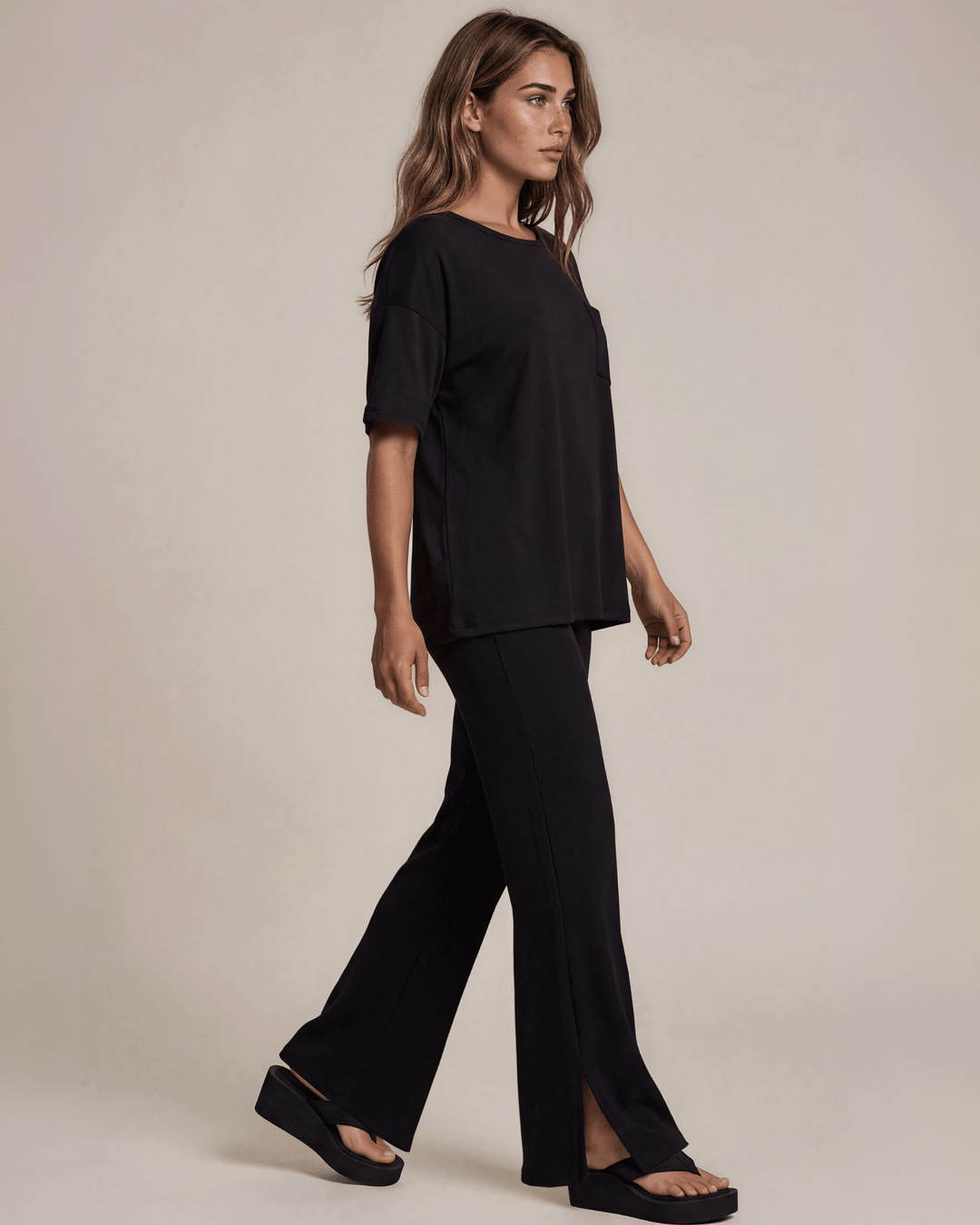 "Black two-piece loungewear set featuring a relaxed-fit short-sleeve crew neck tee with a chest pocket and wide-leg pants with split hems and an elastic waistband, in a soft stretch fabric blend. Made in USA."