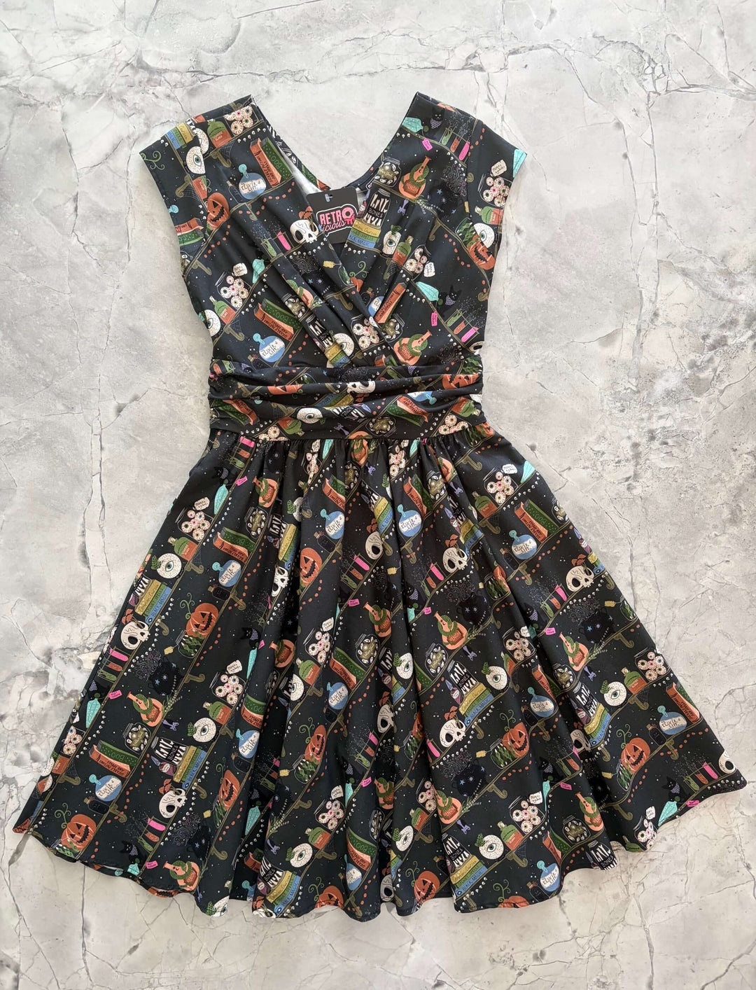 Made in USA, the Retrolicious Potions Greta dress is 100% cotton with a V-neck, gathered waist, pockets, and a true-to-size fit. Sizes XS–4X.